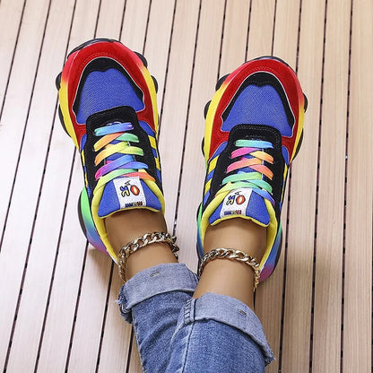 Scarpe da ginnastica multicolore su pavimento in legno, lacci arcobaleno, jeans. Sneakers moda, stile casual, calzature trendy.