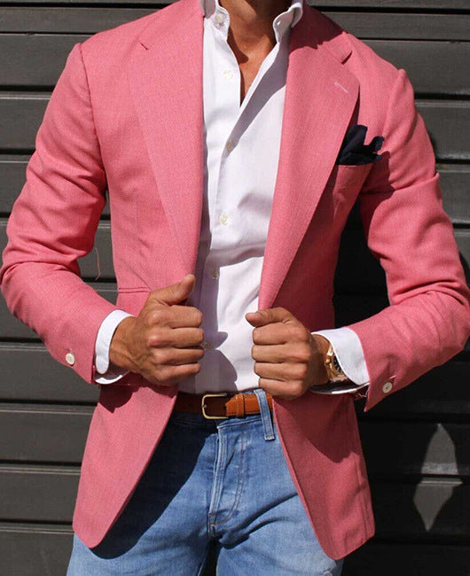 Uomo in giacca rosa elegante, camicia bianca e jeans, posa davanti a sfondo grigio. Moda maschile, abbigliamento casual chic.
