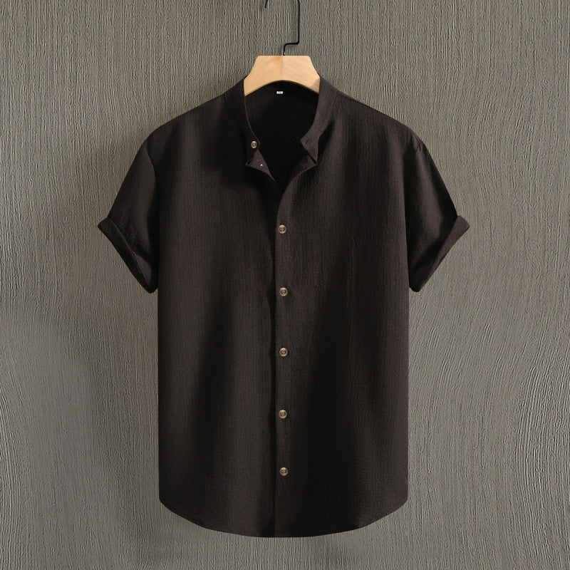 Camicia nera a maniche corte in cotone, design minimalista, bottoni frontali, appesa su gruccia di legno, sfondo grigio testurizzato.