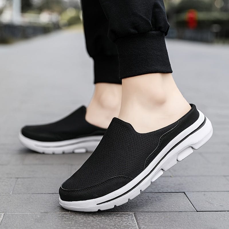 Scarpe slip-on nere da uomo su marciapiede, design casual e sportivo, suola bianca antiscivolo, ideali per passeggiate e tempo libero.