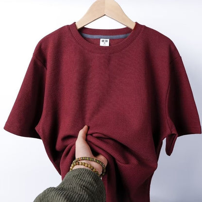 Maglietta rossa a maniche corte su appendiabiti, tessuto a coste, mano che tocca il tessuto. Abbigliamento casual, moda uomo, stile estivo.