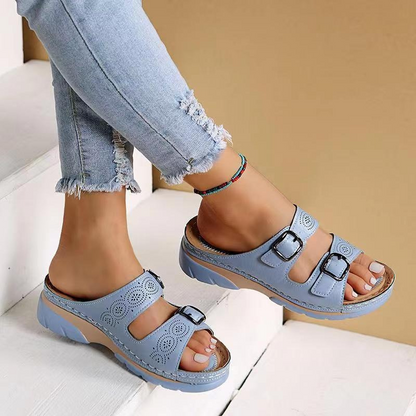 Sandali estivi blu con doppia fibbia su piede femminile, abbinati a jeans strappati. Calzature moda donna, comode e casual per l'estate.