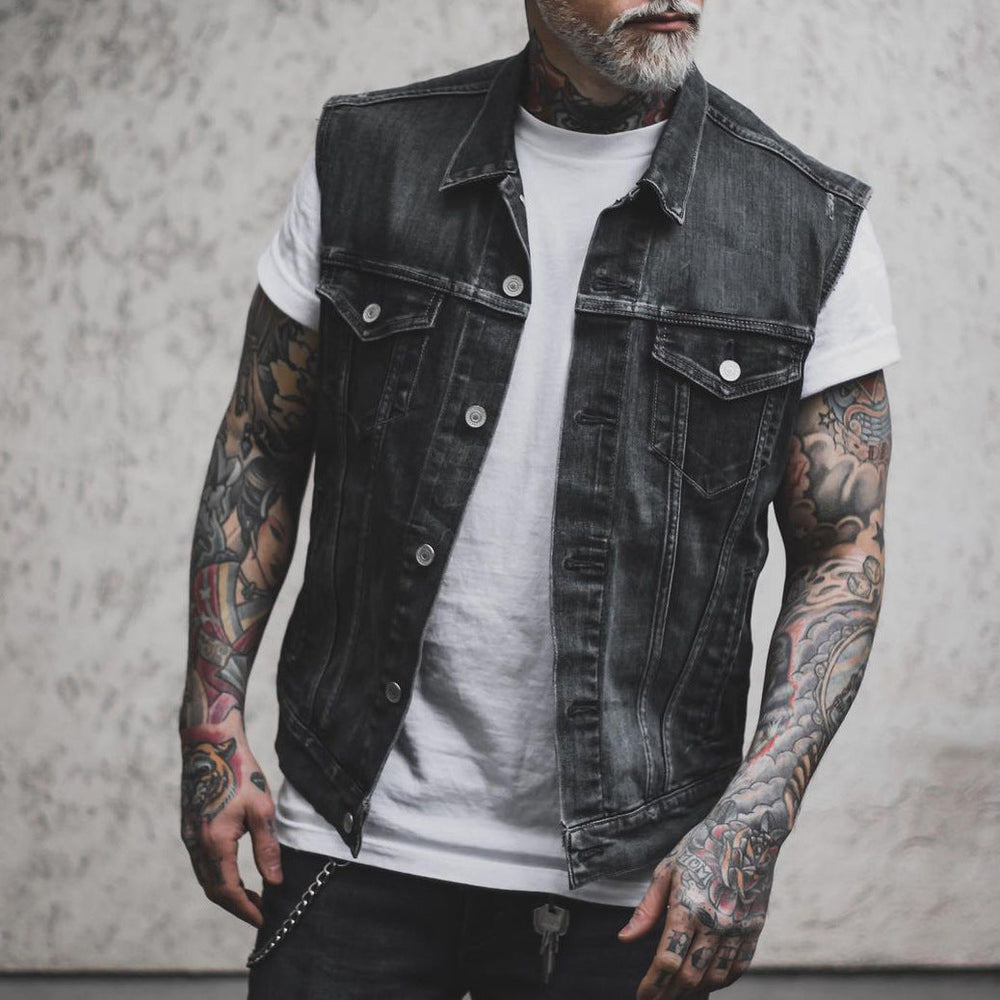 Giacca di jeans nera senza maniche su uomo tatuato, indossa maglietta bianca. Moda streetwear, stile casual, tendenze abbigliamento maschile.