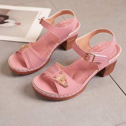 Sandali rosa con tacco largo in legno, cinturino regolabile e dettagli dorati, su pavimento grigio. Scarpe estive eleganti e comode.