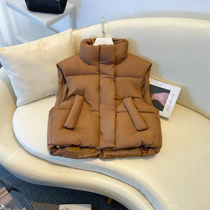 Gilet imbottito marrone su divano bianco, design senza maniche, tasche frontali, ideale per moda autunnale e invernale.