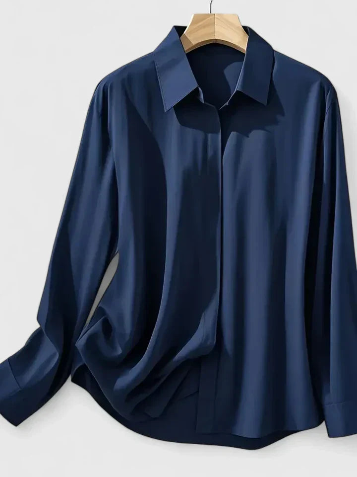Camicia blu scuro in seta, maniche lunghe, colletto classico, appesa su gruccia di legno. Elegante e raffinata, ideale per look formali.