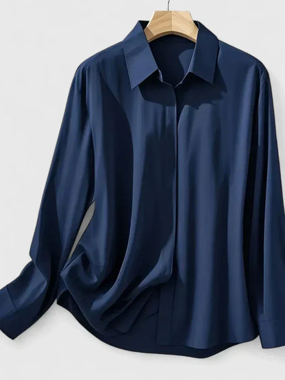 Camicia blu scuro in seta, maniche lunghe, colletto classico, appesa su gruccia di legno. Elegante e raffinata, ideale per look formali.