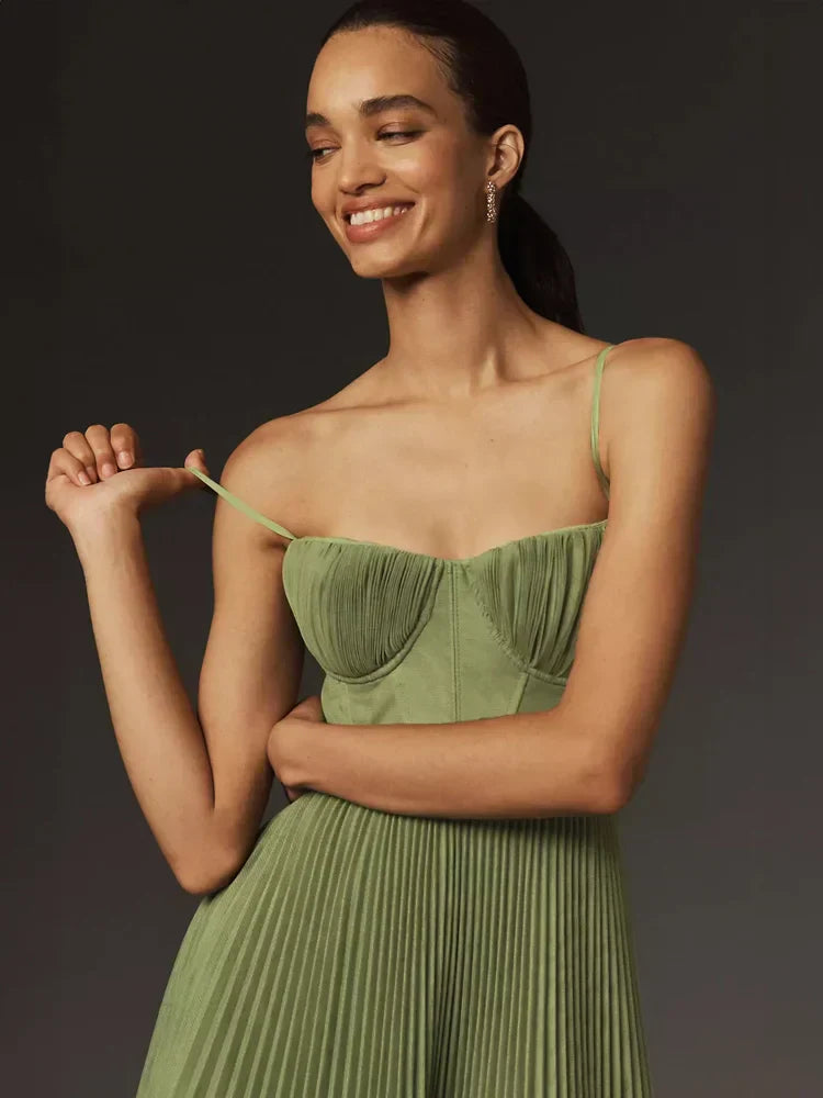 Modella sorridente in abito verde plissettato, spalline sottili, sfondo scuro. Moda elegante, abbigliamento femminile, tendenze 2023.