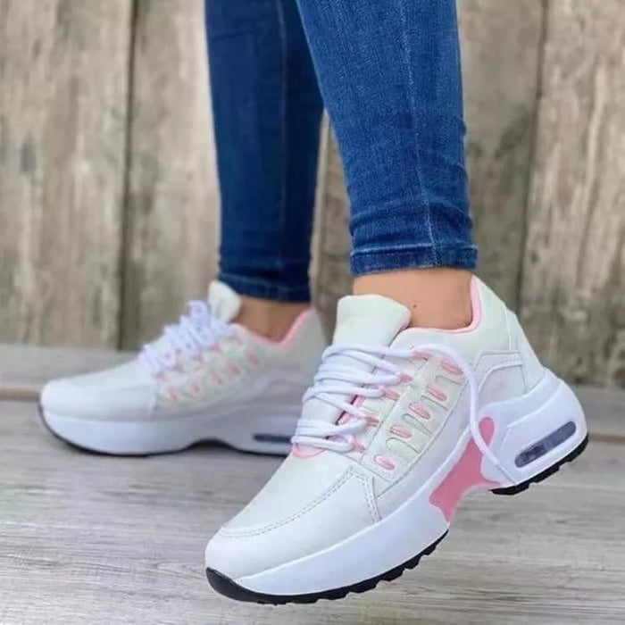 Scarpe da ginnastica bianche e rosa su pavimento in legno, indossate con jeans aderenti. Design moderno, suola spessa, stile casual sportivo.