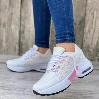 Scarpe da ginnastica bianche e rosa su pavimento in legno, indossate con jeans aderenti. Design moderno, suola spessa, stile casual sportivo.