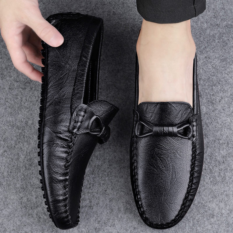 Mocassini uomo in pelle nera con fiocco, suola antiscivolo, indossati su pavimento grigio. Scarpe eleganti e comode per look casual e formali.