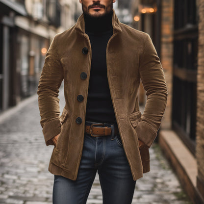 Uomo con cappotto marrone in velluto a coste, maglione nero e jeans, cammina su strada acciottolata. Moda autunnale, stile urbano elegante.