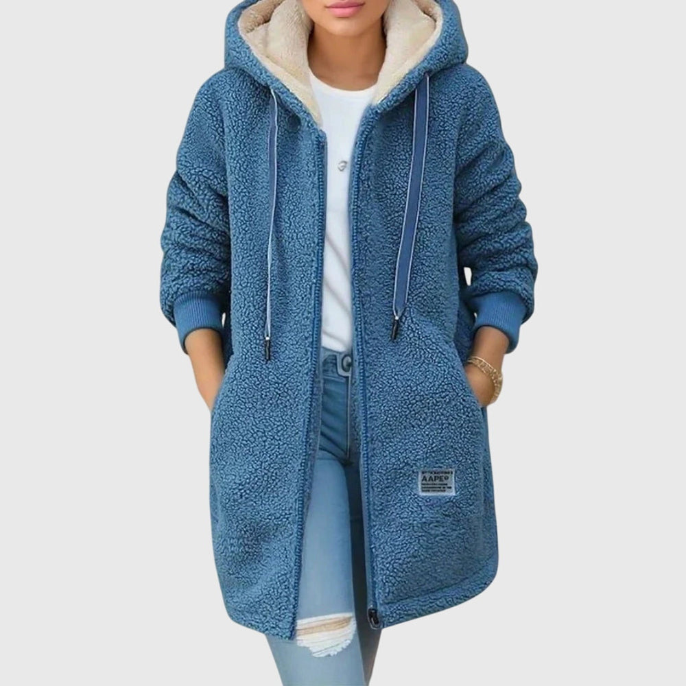 Giacca in pile blu con cappuccio, chiusura a zip, tasche frontali, indossata su jeans strappati e maglietta bianca. Moda casual autunno inverno.