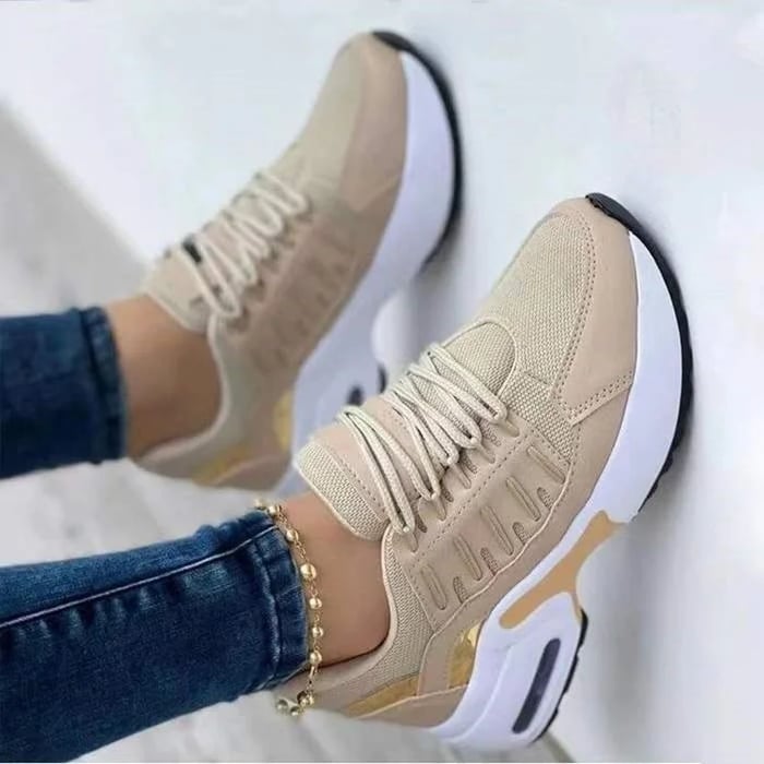 Scarpe da ginnastica beige su sfondo bianco, design moderno con suola bianca e dettagli dorati, indossate con jeans e cavigliera.