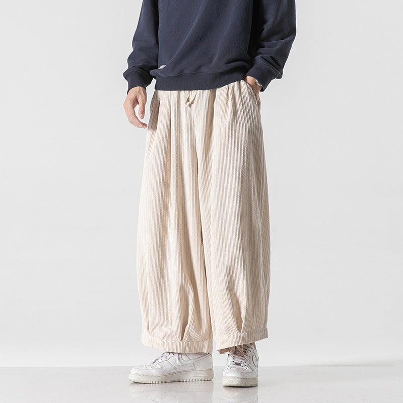 Pantaloni larghi beige uomo, tessuto plissettato, stile casual, abbinati a felpa blu e sneakers bianche. Moda maschile contemporanea.