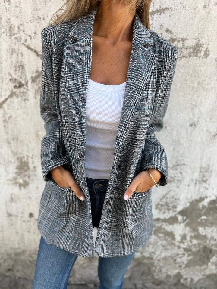 Donna con blazer a quadri grigio, canotta bianca e jeans. Moda autunnale casual, stile elegante e moderno. Sfondo muro grezzo.