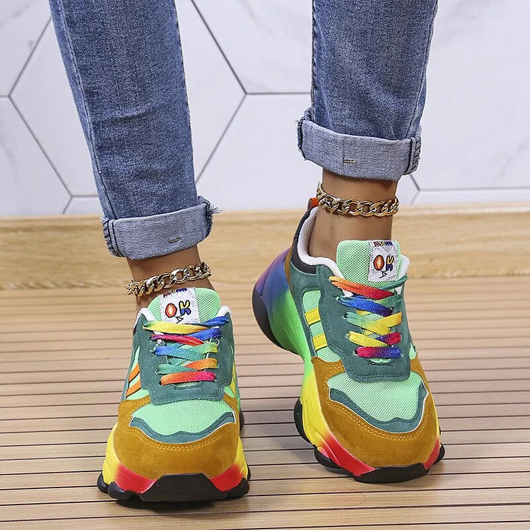 Scarpe da ginnastica multicolore su pavimento in legno, indossate con jeans. Design vivace, suola robusta, perfette per moda casual e streetwear.