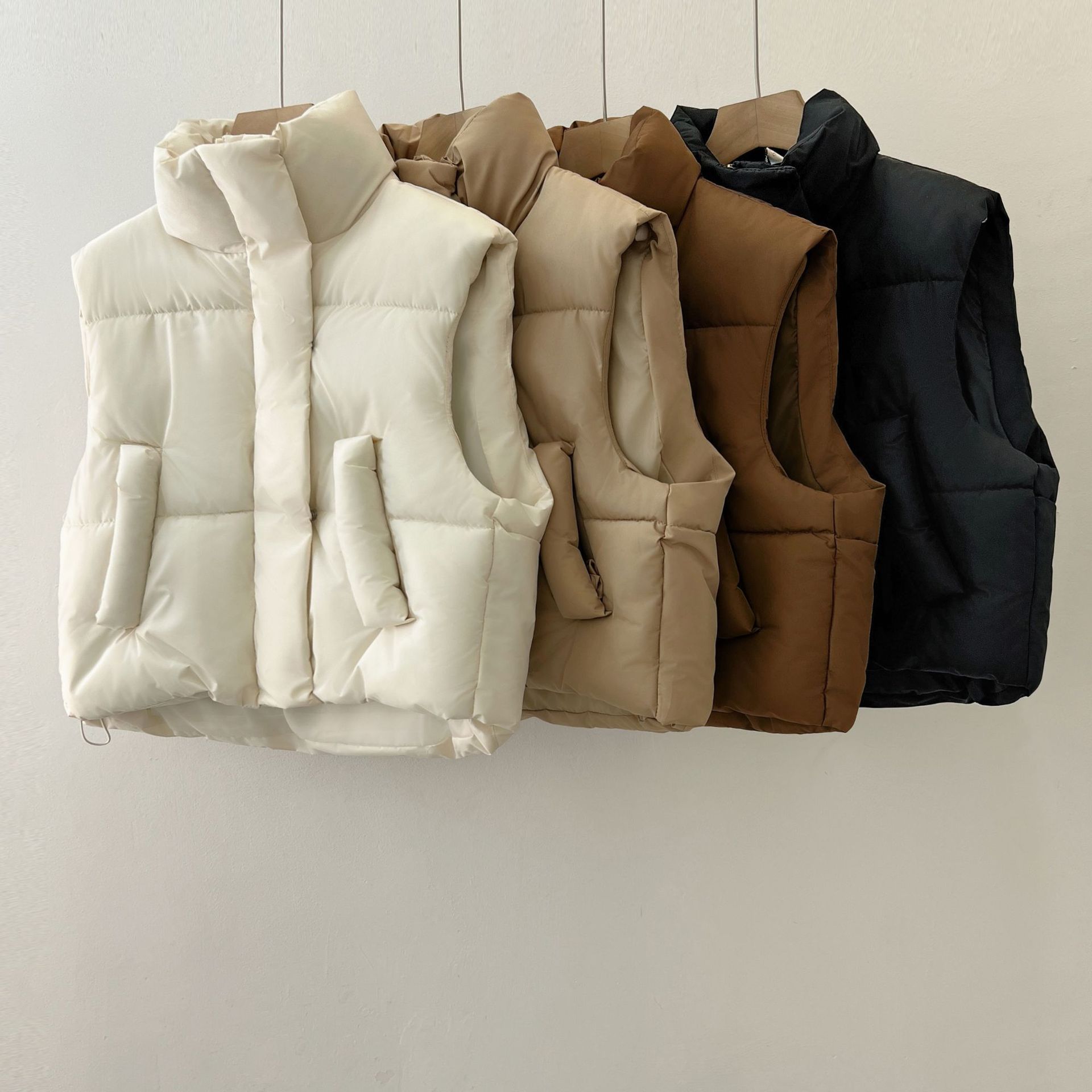 Quattro gilet imbottiti appesi: bianco, beige, marrone e nero. Moda autunno-inverno, abbigliamento casual, giacche senza maniche.