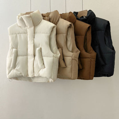 Quattro gilet imbottiti appesi: bianco, beige, marrone e nero. Moda autunno-inverno, abbigliamento casual, giacche senza maniche.
