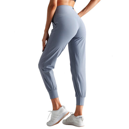 Donna in pantaloni sportivi grigi, scarpe da ginnastica bianche, posa di profilo. Abbigliamento fitness, moda activewear, comfort e stile.