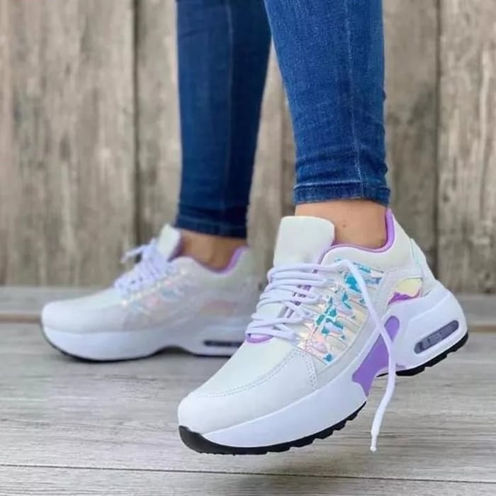 Scarpe da ginnastica bianche e viola con dettagli iridescenti, indossate con jeans aderenti. Scarpe sportive moda donna, su sfondo in legno.