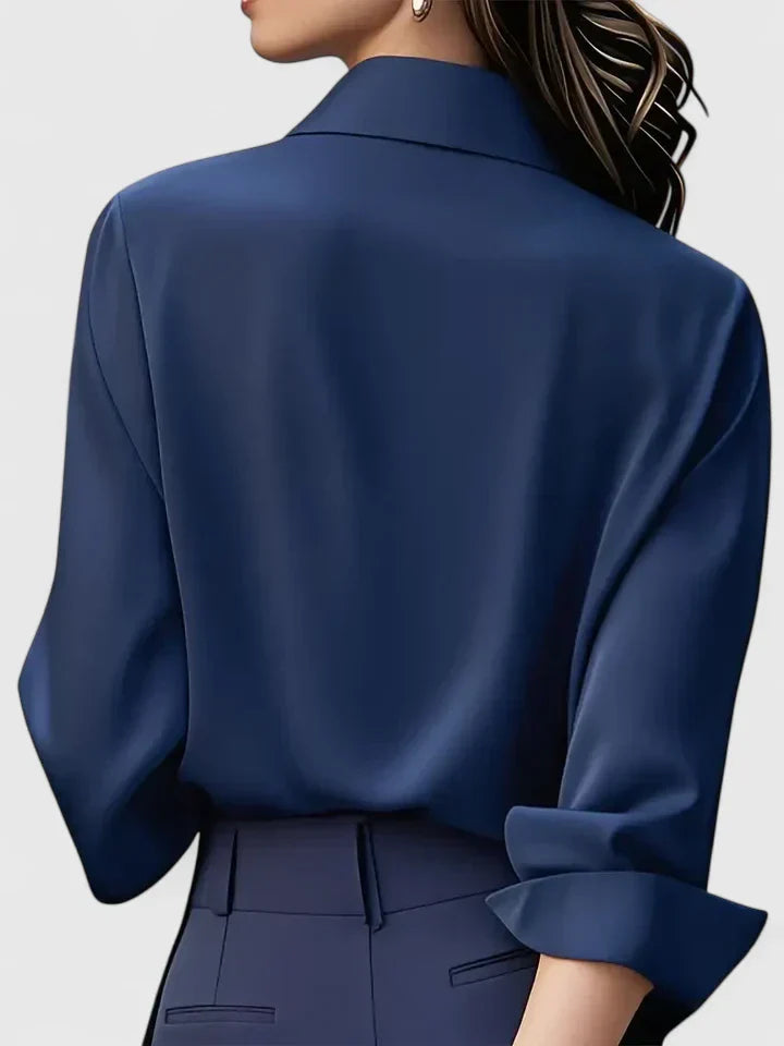 Donna di spalle con camicia blu scuro elegante, maniche arrotolate, abbinata a pantaloni blu. Stile moda femminile, abbigliamento formale.
