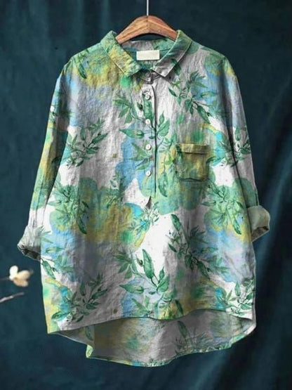 Camicia oversize floreale in lino, colori verde e blu, maniche lunghe, colletto classico, tasca frontale, appesa su sfondo scuro.