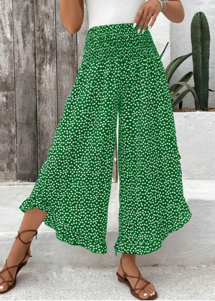 Pantaloni palazzo verdi a pois bianchi, indossati con sandali marroni, sfondo rustico con pianta di cactus. Moda estiva, abbigliamento casual.