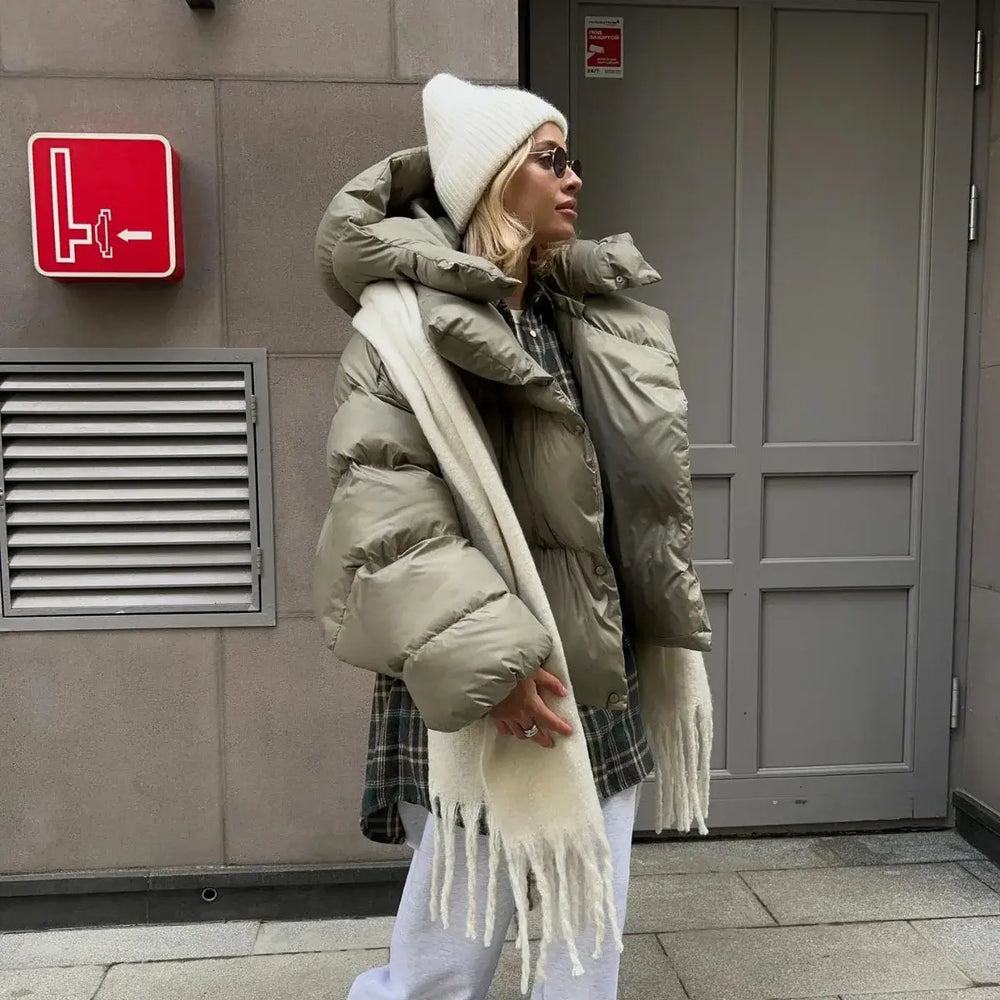 Donna con giacca invernale imbottita verde oliva, cappello bianco e sciarpa, posa all'aperto. Moda invernale urbana, abbigliamento caldo.