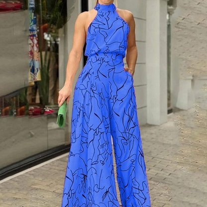 Donna in tuta blu con motivo astratto nero, borsa verde, davanti a una vetrina. Moda estiva elegante, abbigliamento casual chic.
