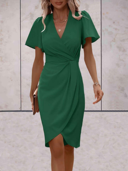 Donna in abito verde elegante, stile avvolgente, con maniche corte e scollo a V, cammina su sfondo neutro. Moda femminile, abbigliamento chic.