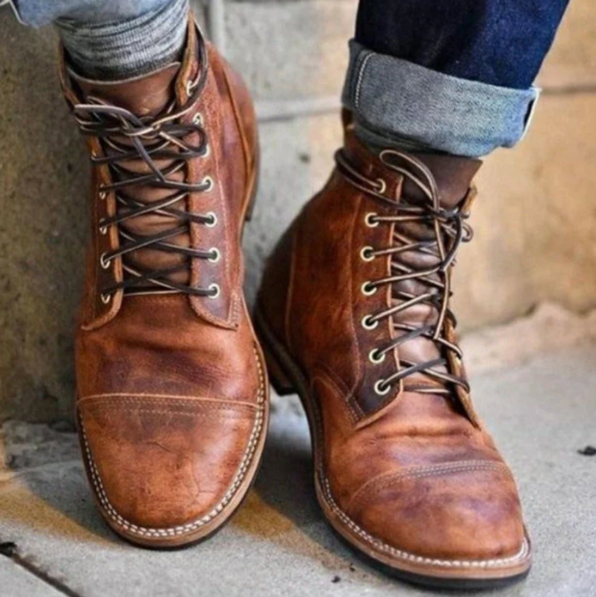 Stivali in pelle marrone da uomo, stile vintage, con lacci e cuciture a vista, indossati con jeans arrotolati. Scarpe eleganti e casual.