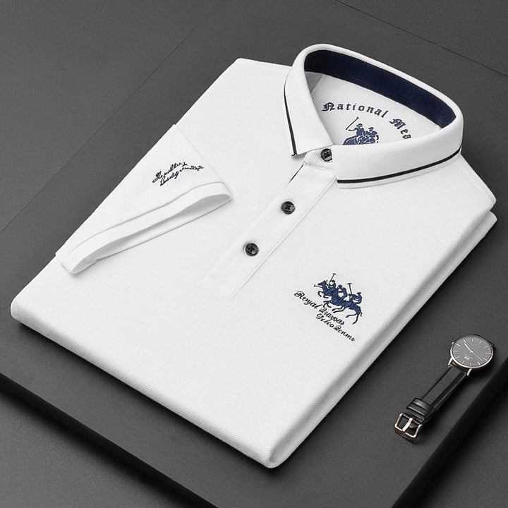 Camicia polo bianca piegata con colletto blu, logo ricamato, orologio nero e cinturino in pelle su sfondo nero. Elegante abbigliamento maschile.