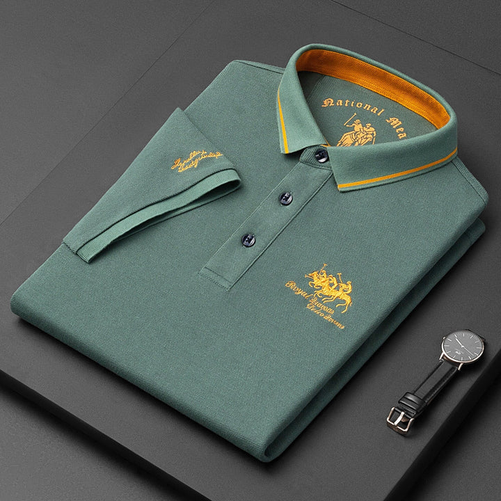 Polo verde piegata con colletto giallo, ricamo dorato "National Hero", orologio nero accanto. Moda uomo elegante, abbigliamento casual di lusso.