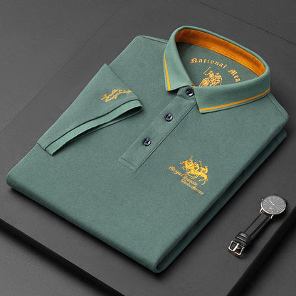 Polo verde piegata con colletto giallo, ricamo dorato "National Hero", orologio nero accanto. Moda uomo elegante, abbigliamento casual di lusso.