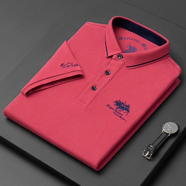 Polo rossa piegata con logo ricamato, colletto a contrasto e orologio nero accanto. Moda uomo elegante, abbigliamento casual di qualità.