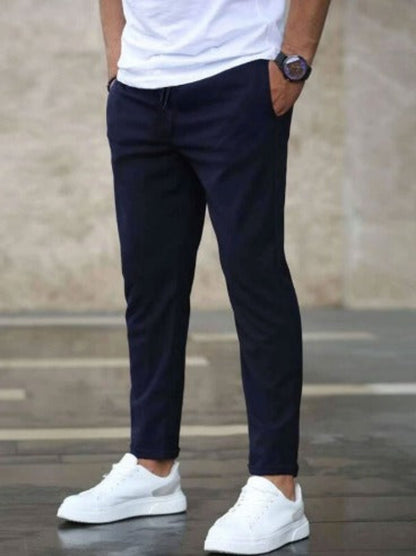 Uomo in pantaloni blu scuro e scarpe da ginnastica bianche, indossa una maglietta bianca. Stile casual, moda maschile, abbigliamento urbano.