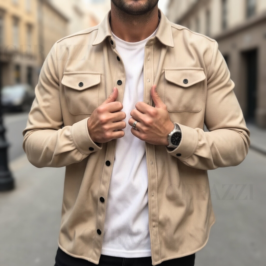 Uomo con camicia beige e t-shirt bianca in strada cittadina, indossa orologio nero e anello argento. Moda maschile casual, stile urbano.