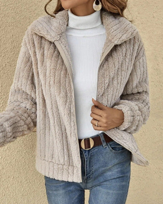 Giacca in pelliccia sintetica beige, indossata su maglione bianco a collo alto, abbinata a jeans blu. Moda autunnale, stile casual chic.