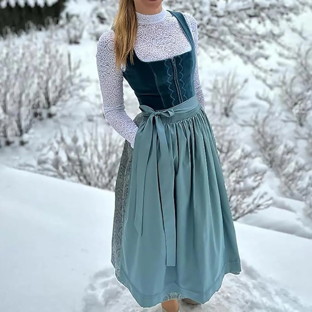 Donna in abito tradizionale tirolese blu e bianco, con corpetto in velluto e gonna ampia, in un paesaggio innevato. Moda invernale alpina.