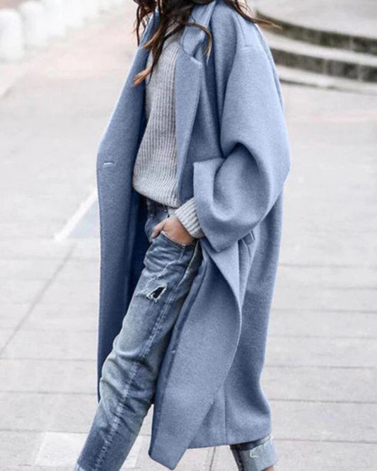 Donna con cappotto lungo blu, maglione grigio e jeans strappati. Moda autunnale casual, abbigliamento femminile elegante e moderno.