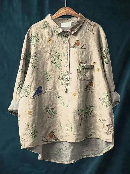 Camicia di lino beige con stampa floreale e uccelli, maniche lunghe, colletto classico, taschino frontale, appesa su sfondo blu.