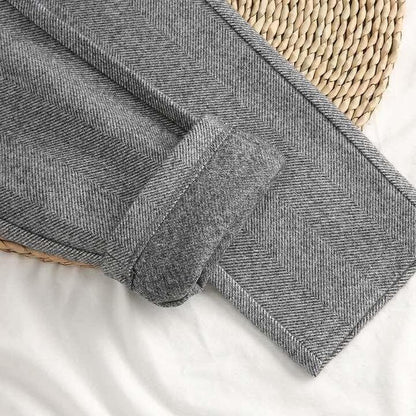 Pantaloni grigi in tessuto a spina di pesce, piegati su un tappetino intrecciato. Stile elegante, moda autunno-inverno, abbigliamento uomo.