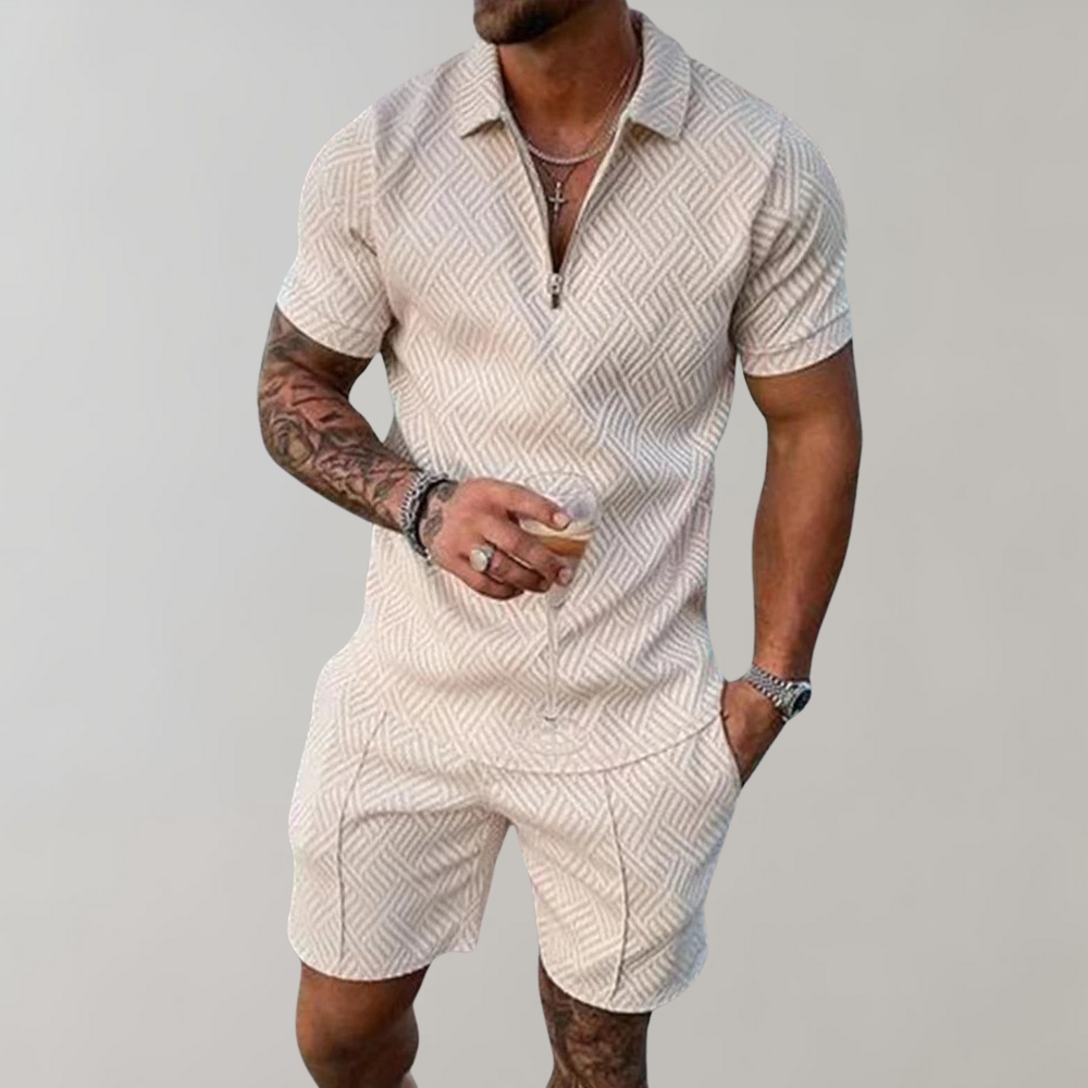 Uomo con tuta estiva beige a motivi geometrici, maniche corte, con bicchiere in mano. Moda maschile casual, abbigliamento estivo elegante.