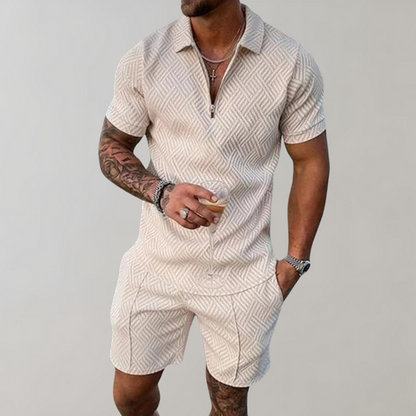 Uomo con tuta estiva beige a motivi geometrici, maniche corte, con bicchiere in mano. Moda maschile casual, abbigliamento estivo elegante.