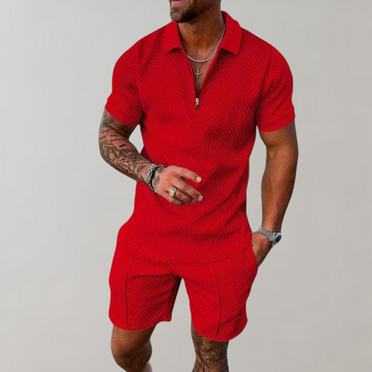 Uomo in tuta rossa a maniche corte con motivo geometrico, indossa collane e orologio. Moda estiva maschile, abbigliamento casual elegante.