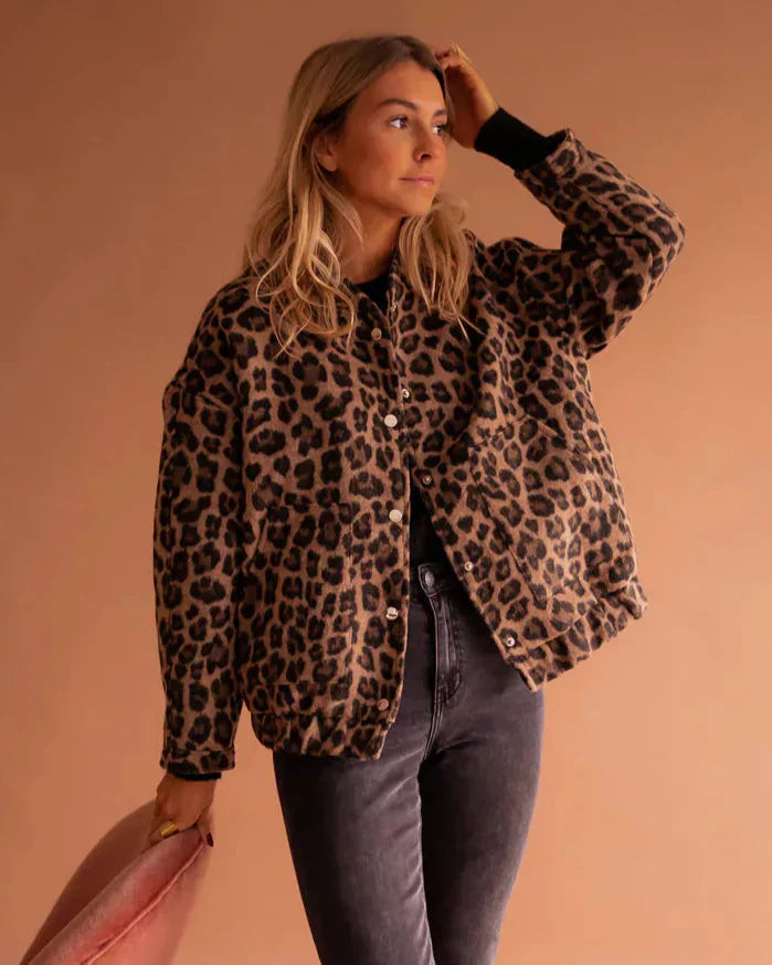 Donna con giacca leopardata, jeans grigi e capelli biondi, posa su sfondo beige. Moda autunnale, stile casual chic, tendenze abbigliamento 2023.