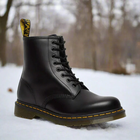 Stivale Dr. Martens nero su neve, design classico con cuciture gialle, suola robusta. Scarpe iconiche per moda invernale e stile urbano.