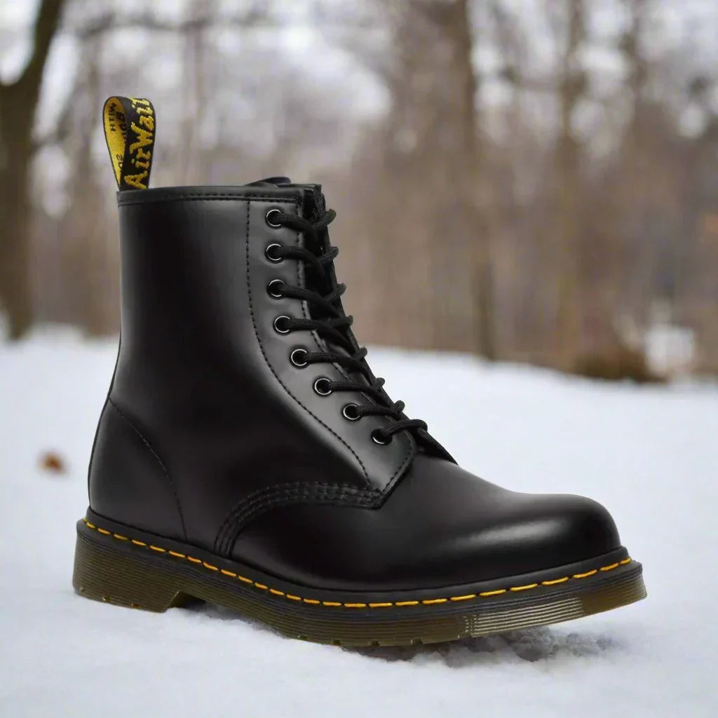 Stivale nero Dr. Martens su neve, design classico con cuciture gialle, allacciatura alta, suola robusta. Scarpe iconiche moda invernale.