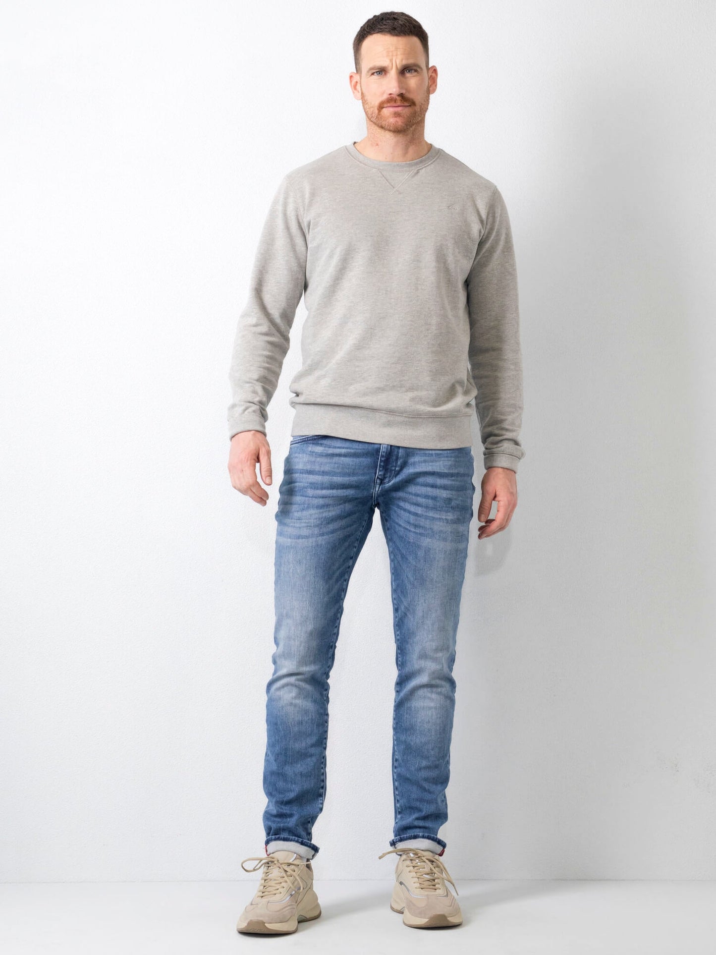 Uomo in jeans blu e maglione grigio, posa su sfondo bianco. Moda casual maschile, abbigliamento autunnale, stile moderno.